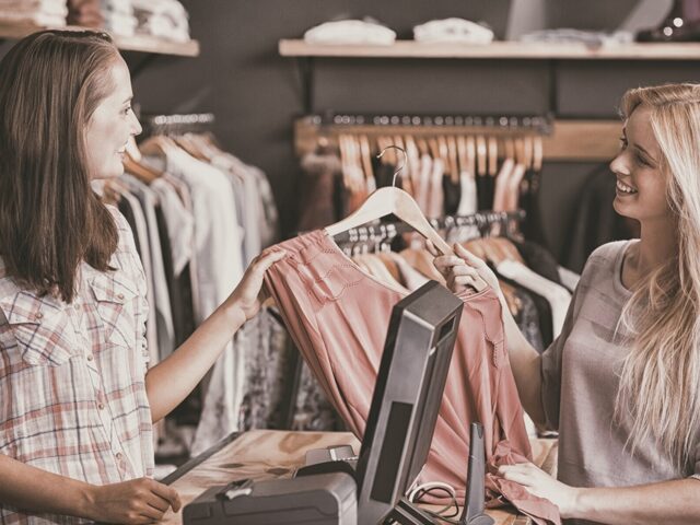 Young woman at clothing store checkout hands shirt to sales associate 978b8d064138018a1dfad71b9882dd21